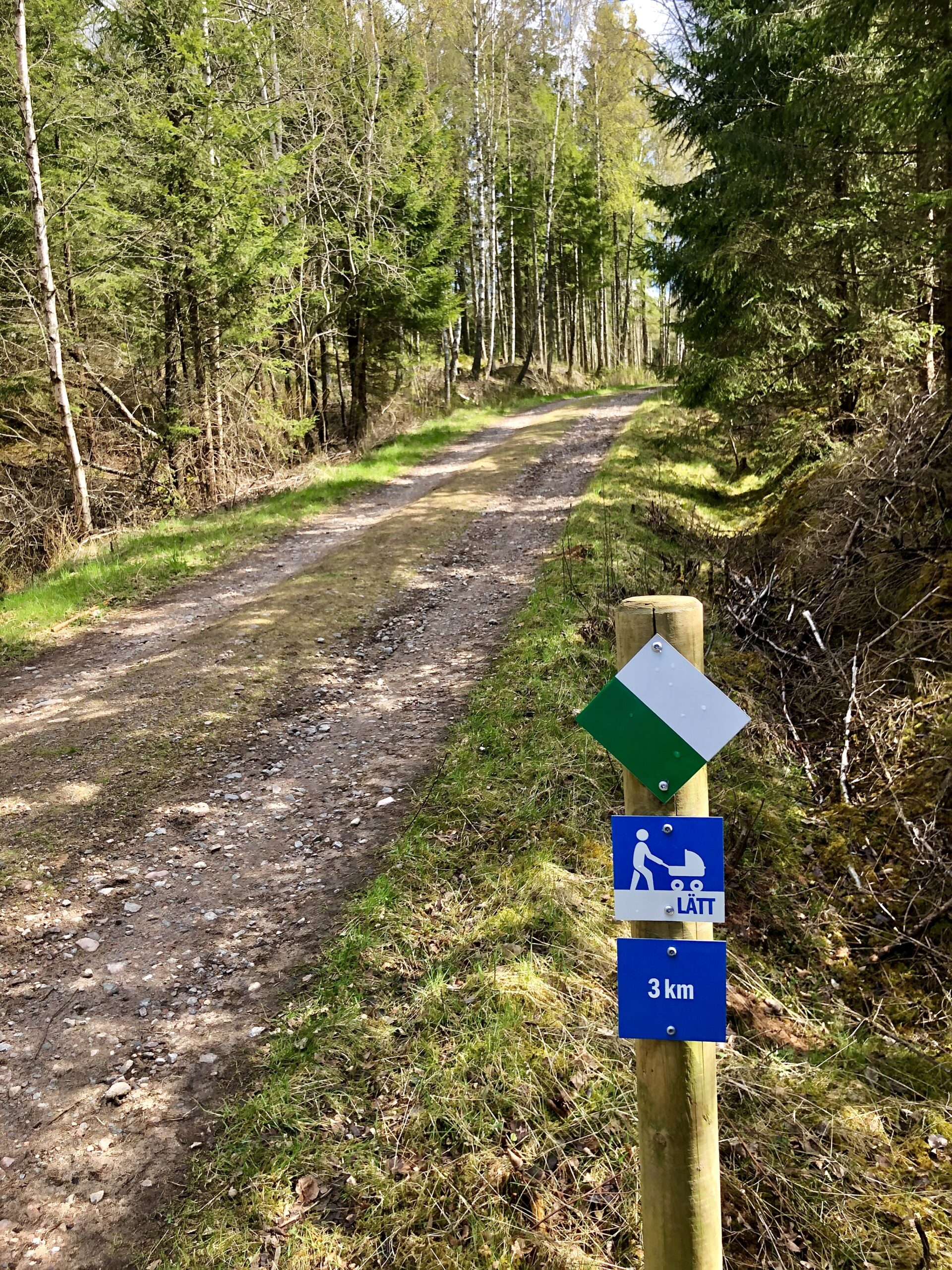 Vandringsled mellan Hestraviken och Isaberg, grusväg kantad av skog och med markering som antyder att det är en lätt led där familj med vagn kan gå