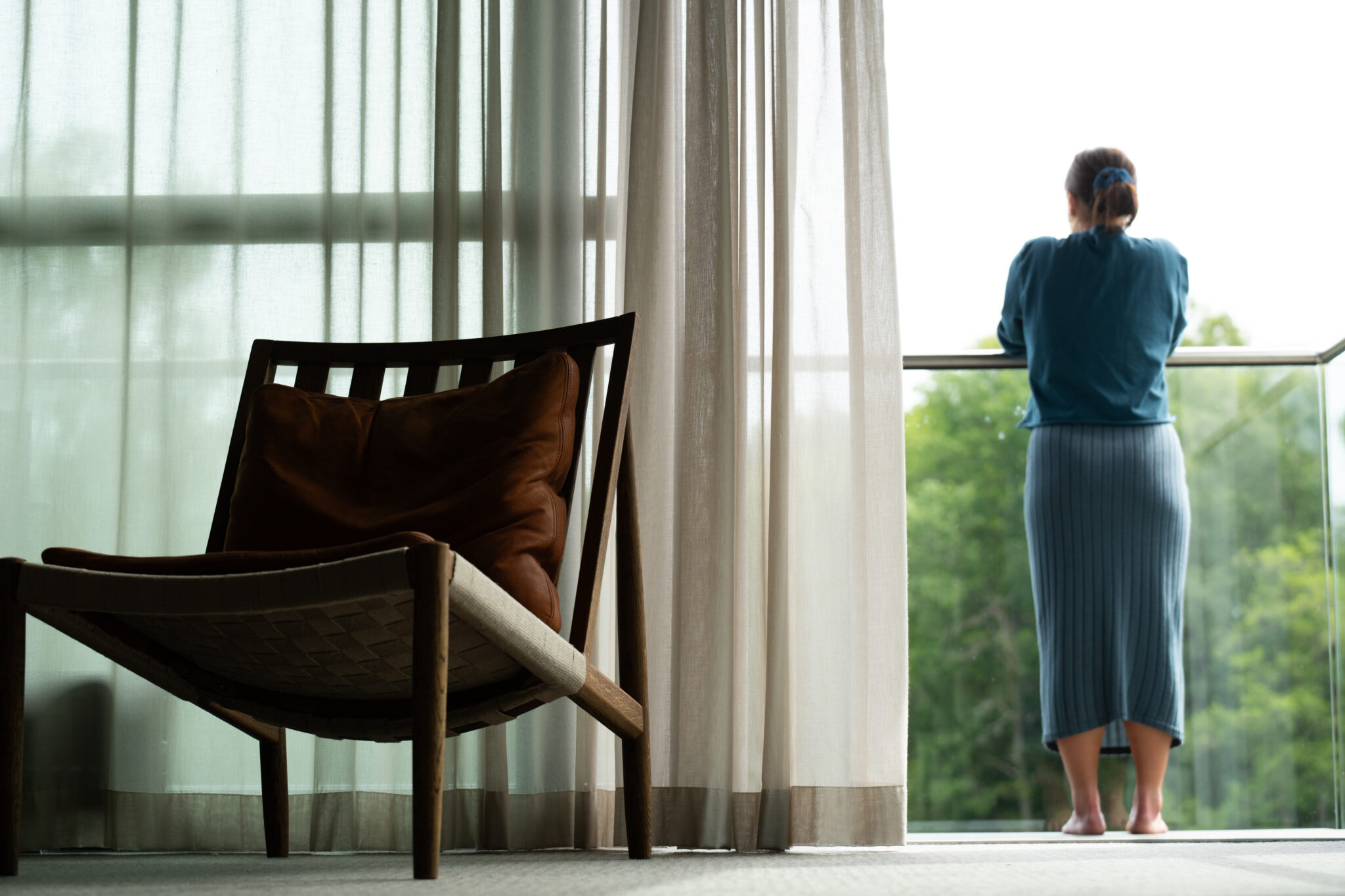 Kvinna på balkongen i ett av våra Deluxerum i Riverside Spa Villan, hon kikar ut över ån Nissan med grönskande skog på andra sidan ån, vilsam fåtölj att sitta i förgrunden