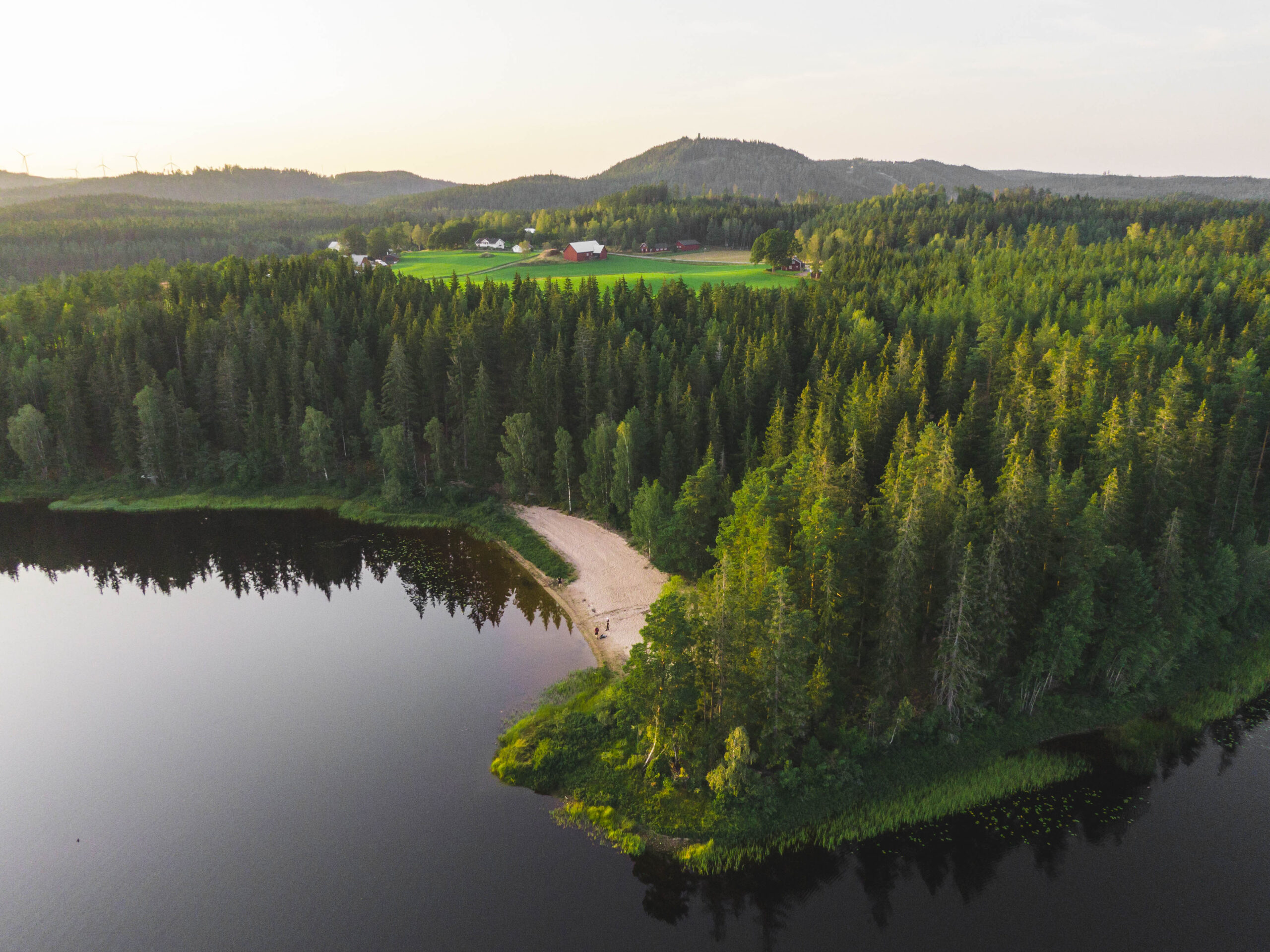 Flygfoto över Vik vid Hestraviken hotell, med utsikt över ängar, sandstrand, Algustorpasjön och Isaberg, en plats för hållbarhet och naturupplevelse.