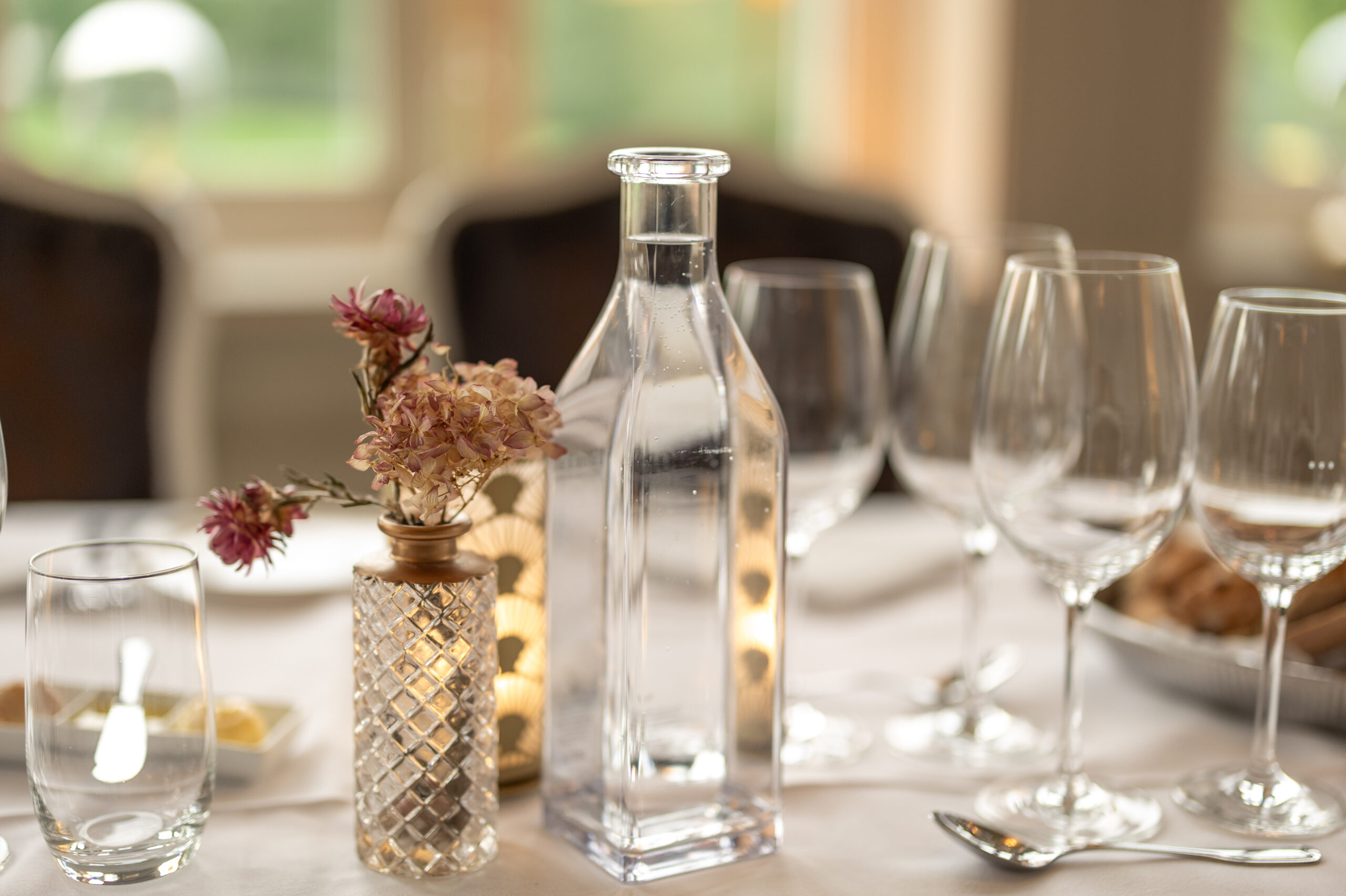Välkommen till bords, glasflaska med kolsyrat vatten, vin- och vattenglas samt linte vas med torkade eterneller