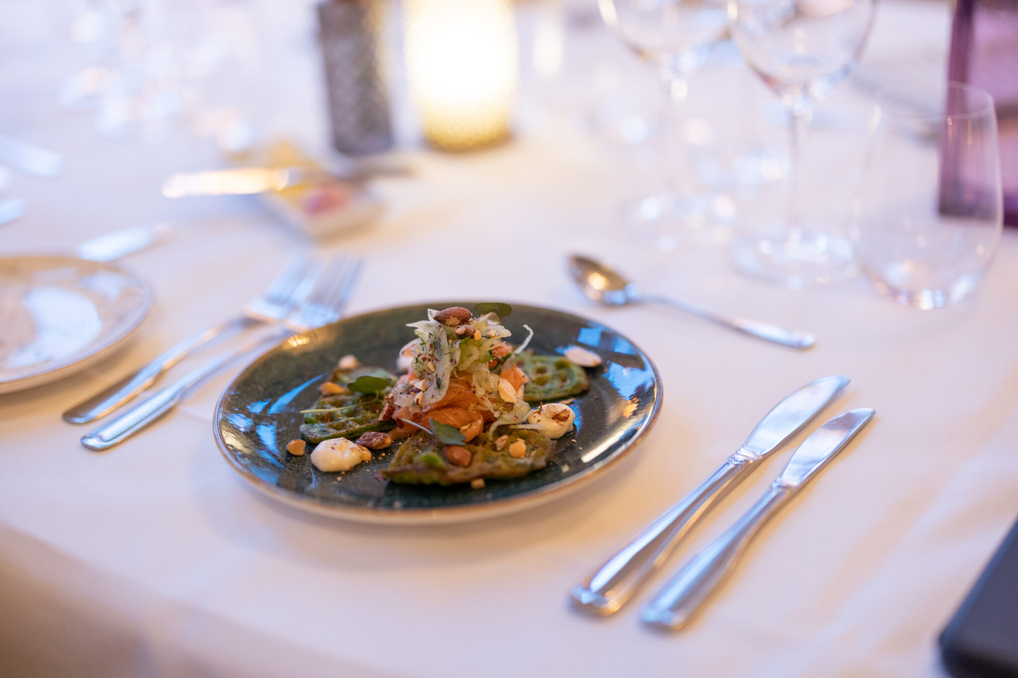 Förrätt framdukad till gäst på turkos tallrik, putsade silver bestick och vikt linneservett vid sidan om
