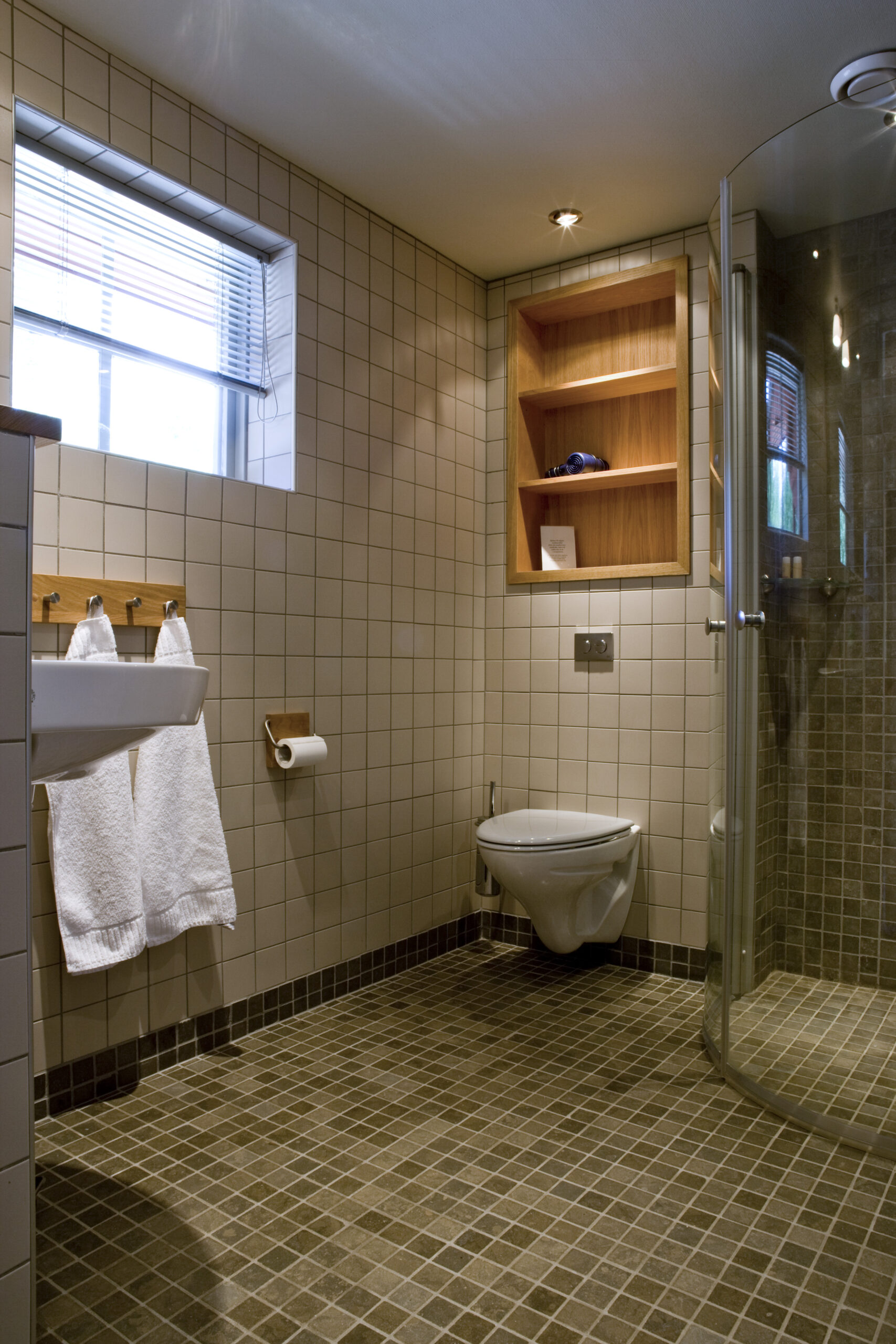 Interiör badrum, dusch med glasväggar, vägghämgd wz, handfat och infälld hylla i ek för dina hudvårdsprodukter allt i våra Deluxe rum i Villa 4