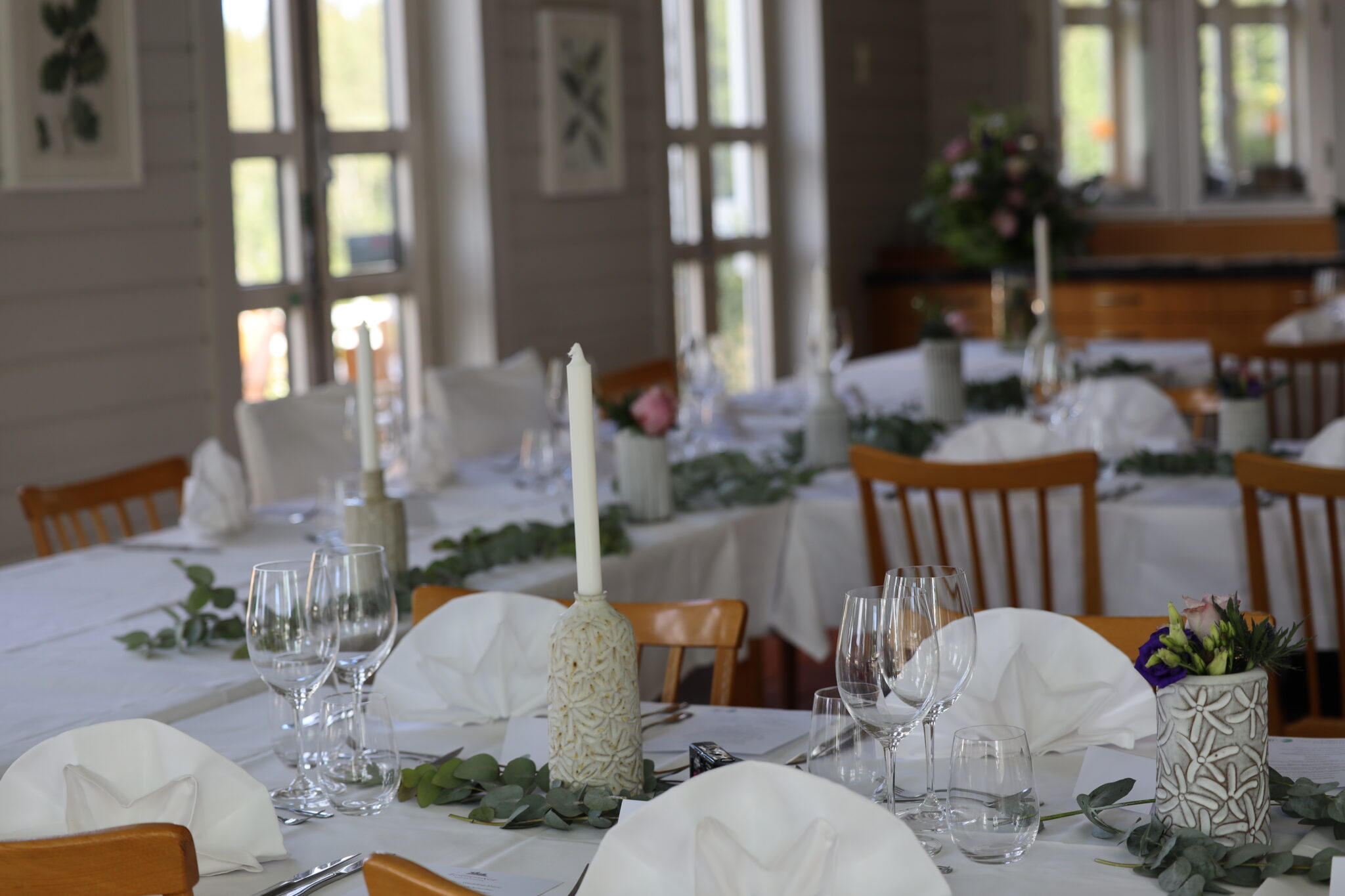 Matsal dukad för bröllop, vita linneservetter och vita linnedukar, eukalyptus dekorerar borden och vita stearinljus i lokal producerade vaser och ljushållare
