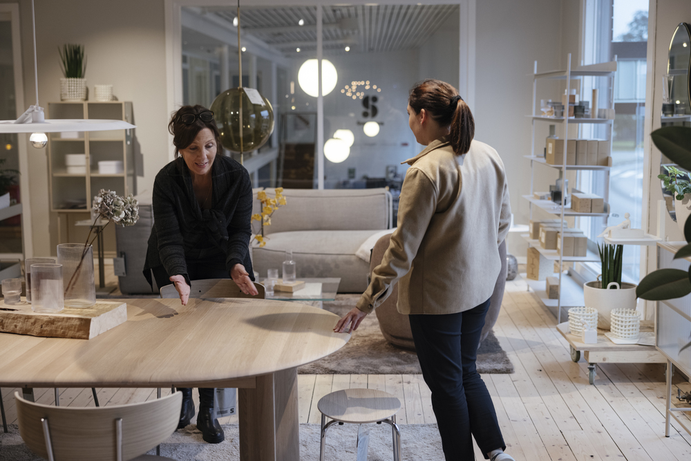 Två kvinnor samtalar vid ett bord i en butik som säljer skandinaviska design möbler, inredning och armaturer