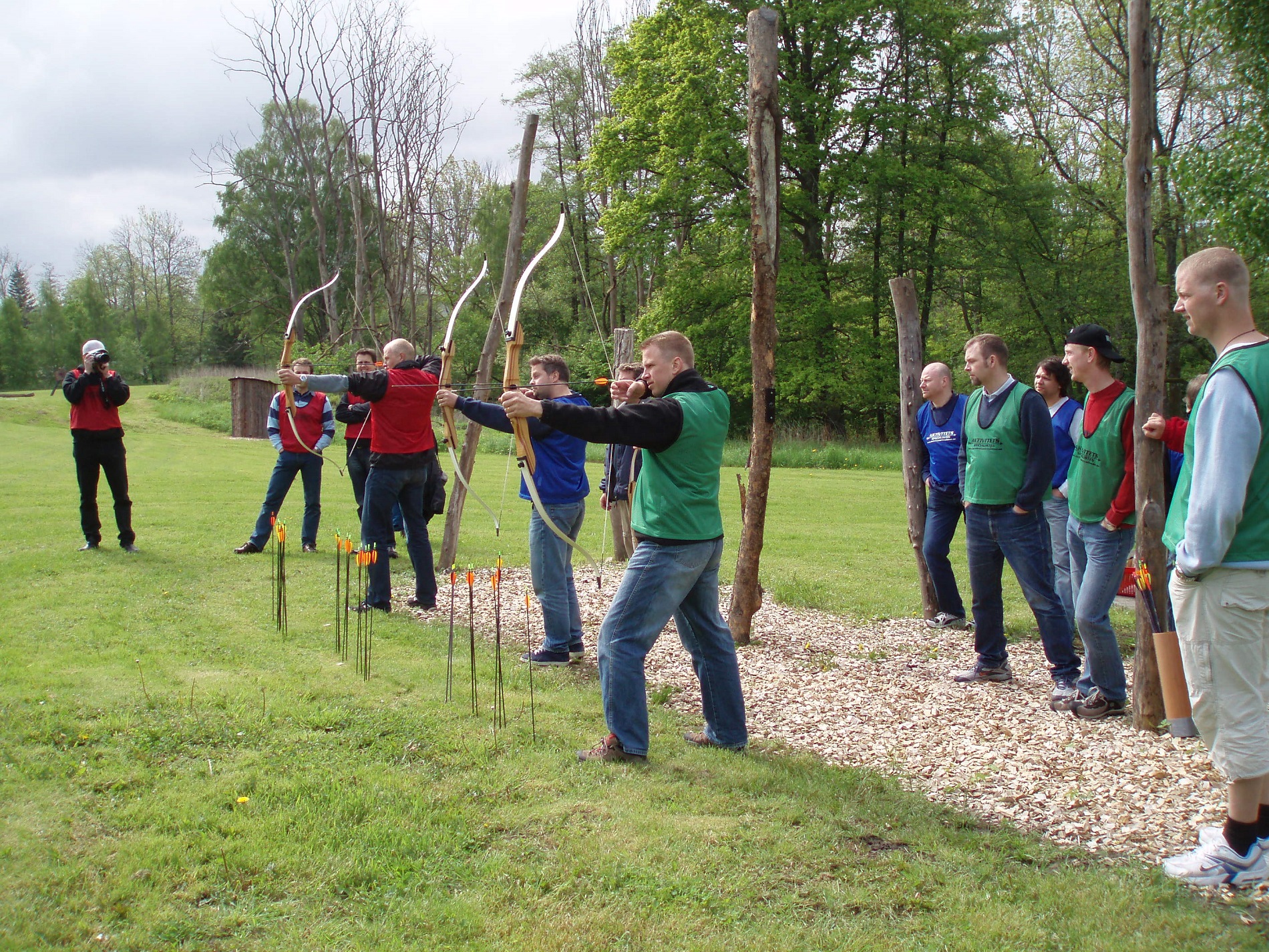 Konferensdeltagare i färd med att skjuta pilbåge, deras kollegor står bakom dem och hejjar på