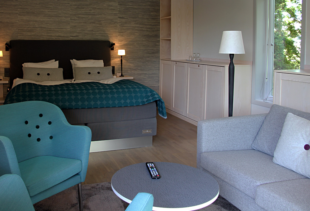 Interiör Deluxerum Villa 5 med dubbelsäng, extrasäng i sängskåp samt sittgrupp med soffa och fåtöljer