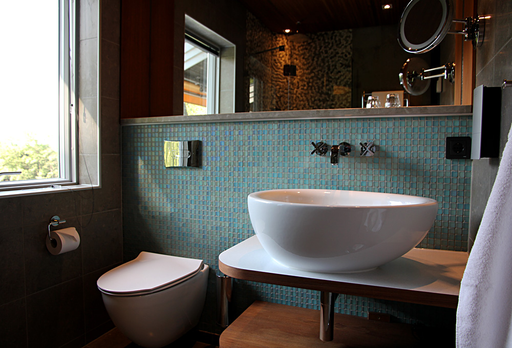 Badrum med handfat, wc-stol, generös spegel samt fönster mot Nissan på Hestraviken hotell och spa vid Isaberg i Småland