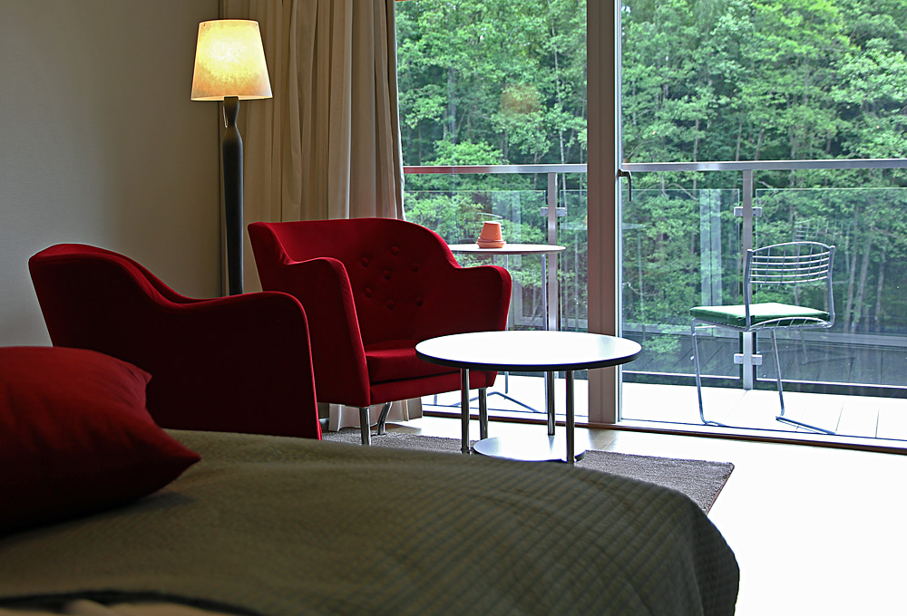 Dubbelsäng med panoramafönster, sittfåtöljer samt balkong med möbler från Grythyttan och utsikt över Nissan i våra Dubbelrum Riverside i Villa 5