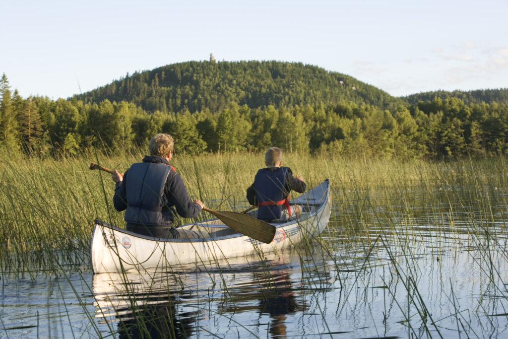 Två personer paddlar kanot på Algustorpasjön med Isabergs skogsklädda berg i bakgrunden.