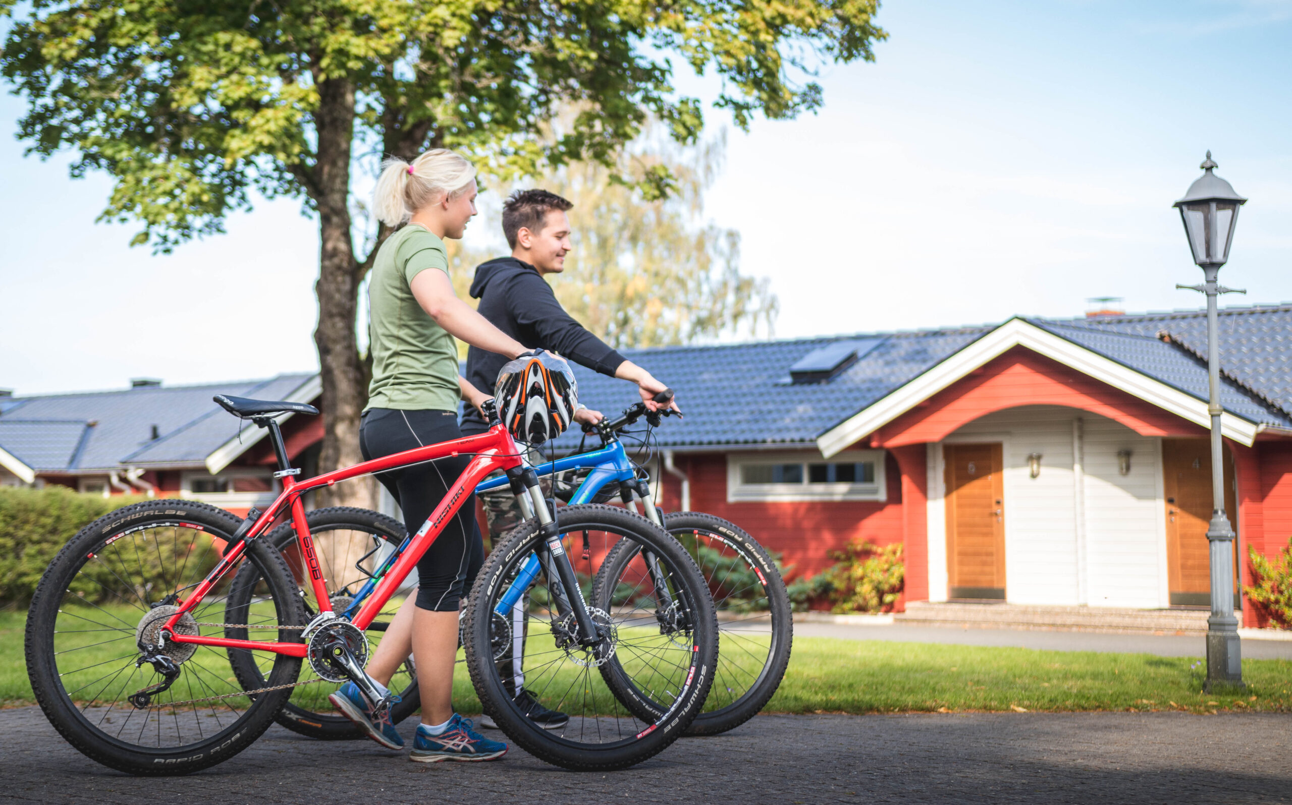 Tjej och kille med mountainbike i trädgården på Hestraviken, framför en av hotellrumsbyggnaderna