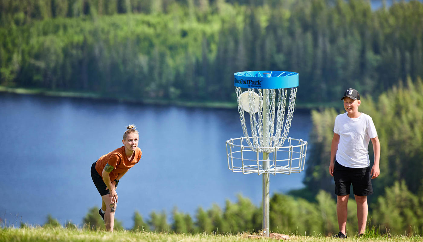 Två ungdomar spelar discgolf på Isaberg, med den vackra utsikten över Algustorpa sjön i bakgrunden. En perfekt aktivitet för både nybörjare och erfarna spelare i Småland.