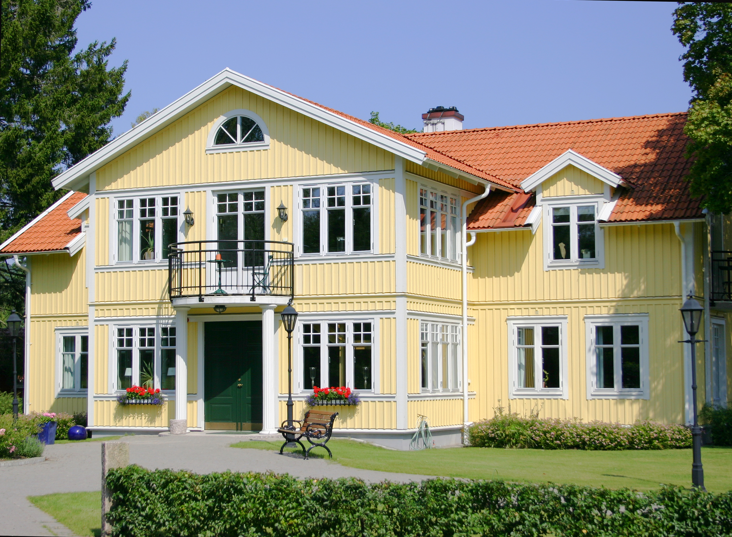 Herrgårdsvillan som erbjuder dubbelrum superior, juniorsviter och svit penthouse en solig sommardag med sommarblomster i balkonglådorna